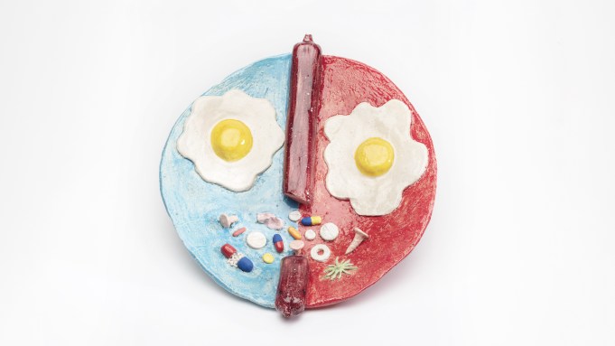 A ceramic plate with two ceramic fried eggs that look like fries and colorful ceramic pills that look like a mouth.