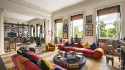 a room with large windows, sofas, and many paintings on the wall.