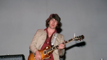 A man holding a guitar before an amp.