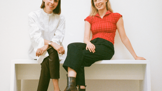 Two smiling women sit on a bench.